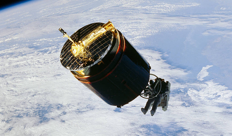 Astronaut holding on to the bottom of the satellite, above Earth